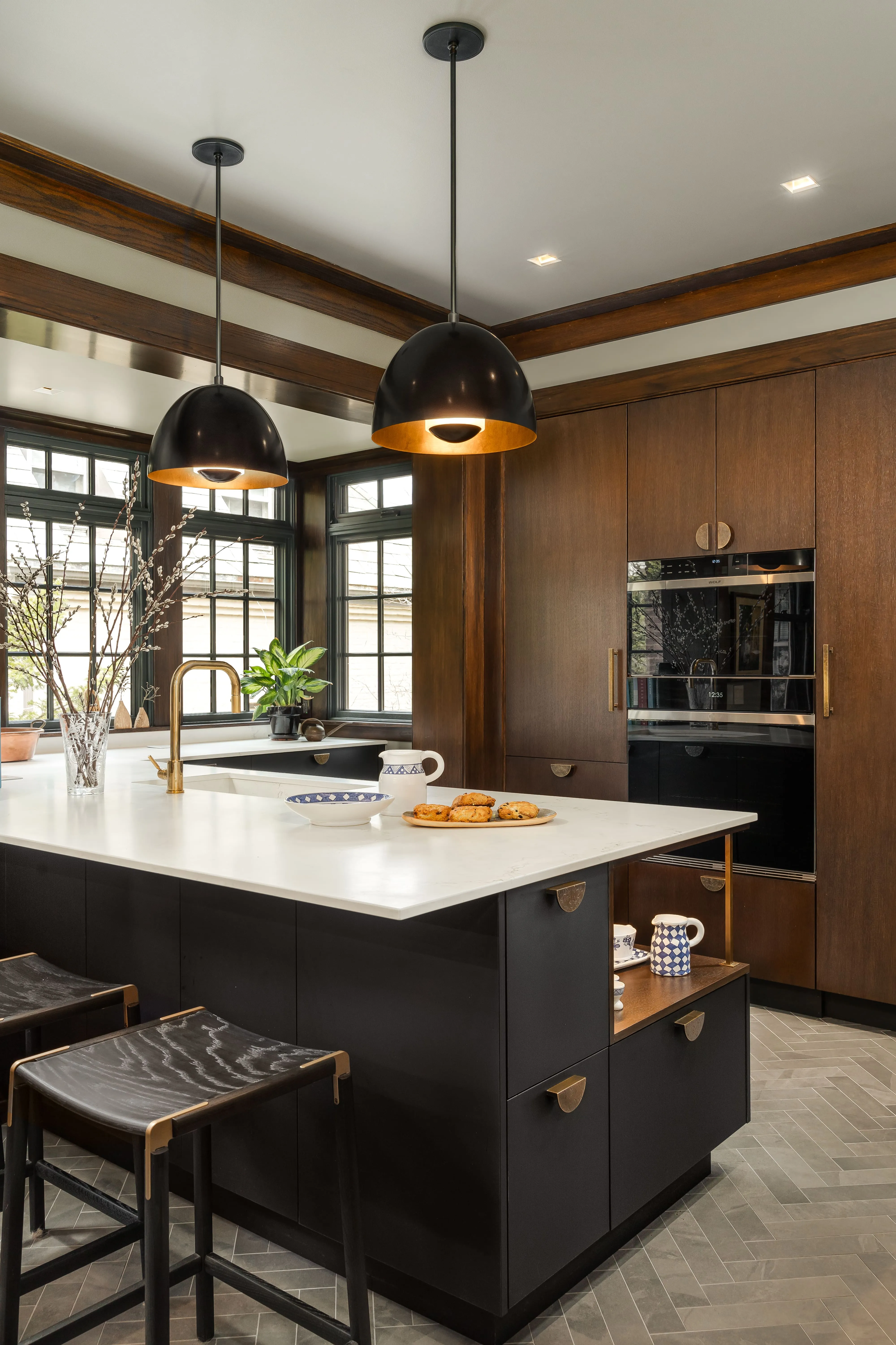 Modern kitchen with dark wood cabinetry, black island with white countertop, two black pendant lights, and bar stools.