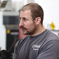 Man with short hair and beard wearing a gray sweatshirt looking to the side in an indoor setting.