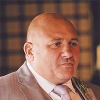 Portrait of a bald man in a suit with a pink tie, looking sideways.