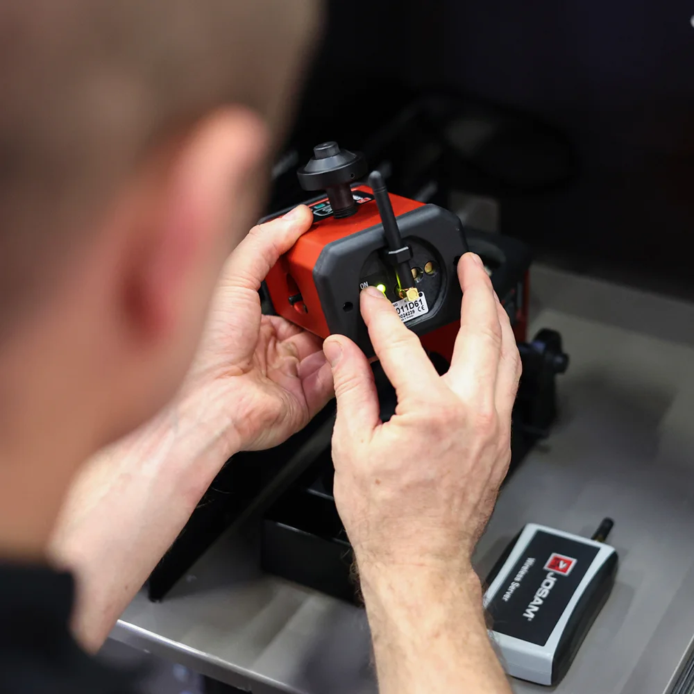 Person holding and adjusting a red electronic device with antenna and indicator light.