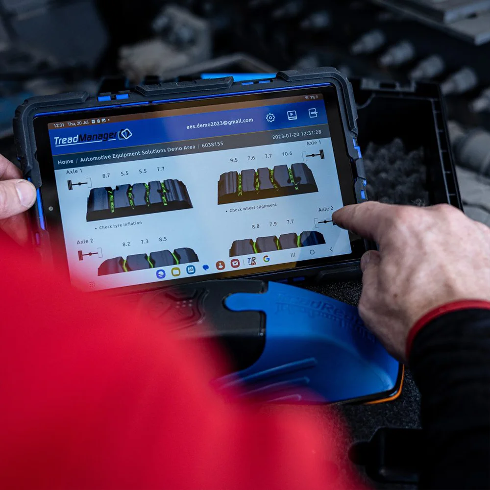 Person using a rugged tablet showing TreadManager software with tire tread measurements and wheel alignment data for axle 1 and axle 2.