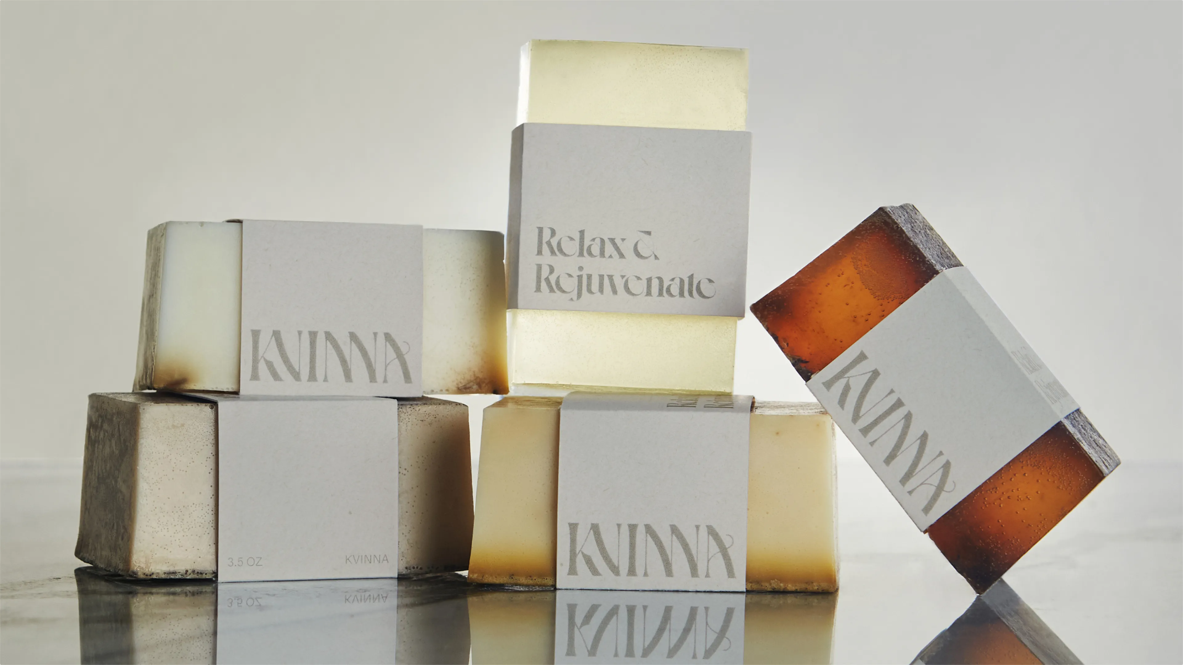 Kvinna Relax and Rejuvenate artisan soap bar collection in amber and cream tones with branded paper labels arranged on reflective white surface, packaging designed by Unbound Collective