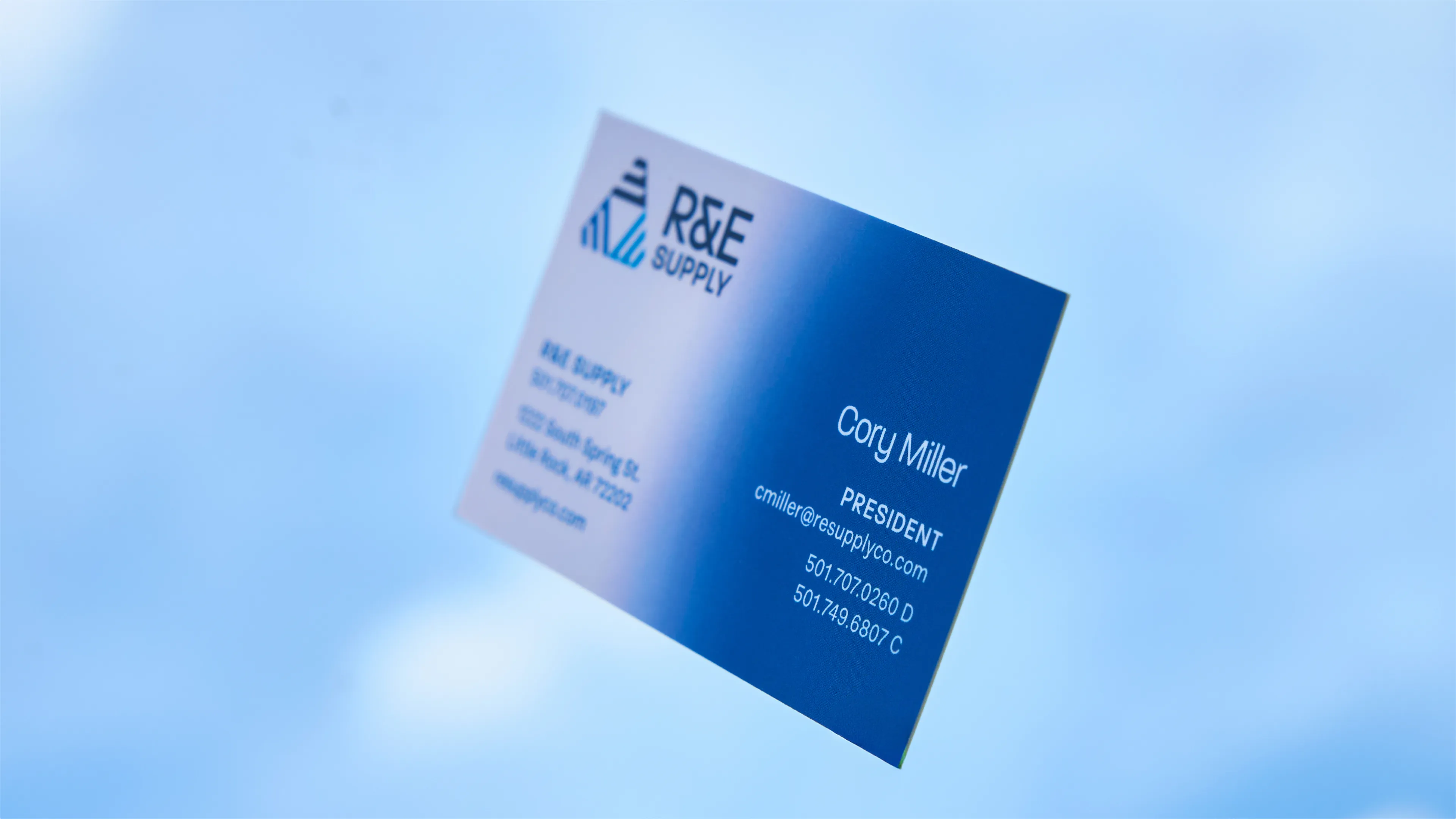 R&E Supply white to blue gradient business card for Cory Miller President floating against blue sky, print design by Unbound Collective