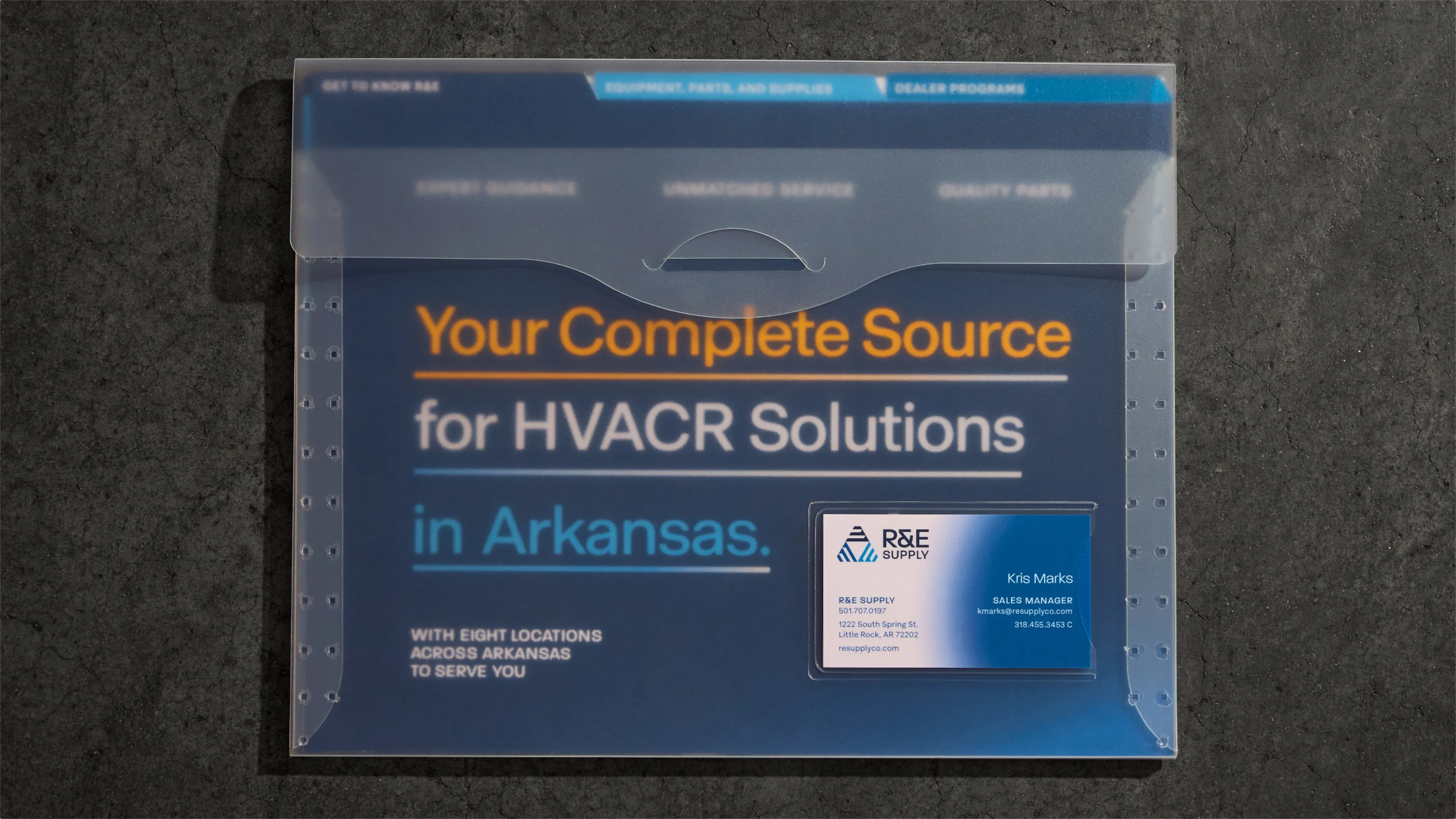 R&E Supply Your Complete Source for HVACR Solutions in Arkansas sales folder with Kris Marks Sales Manager business card tucked in pocket on dark concrete surface, print design by Unbound Collective