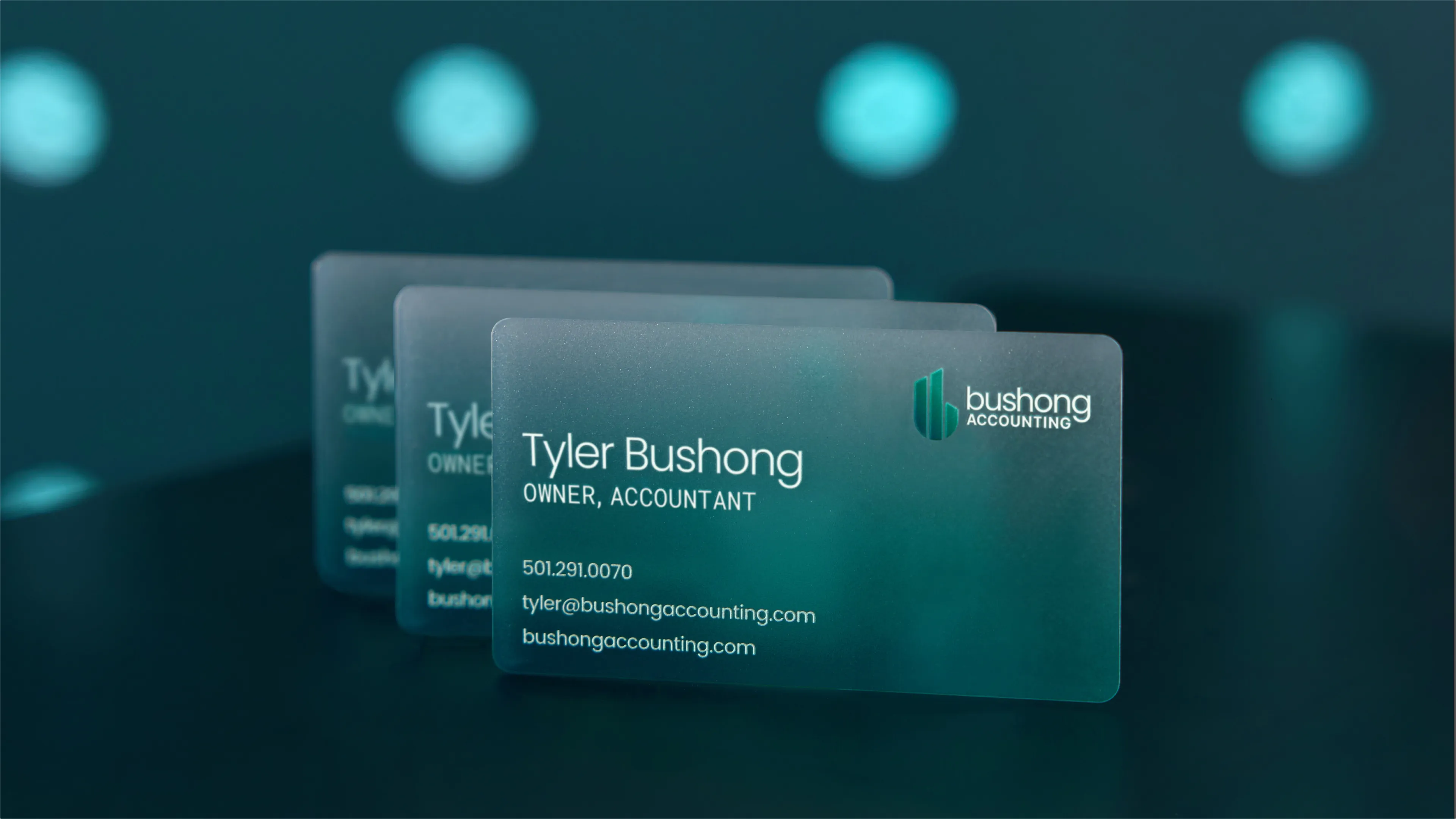 Bushong Accounting frosted teal business cards for Tyler Bushong Owner Accountant in widescreen 3D render against teal bokeh background, print design by Unbound Collective