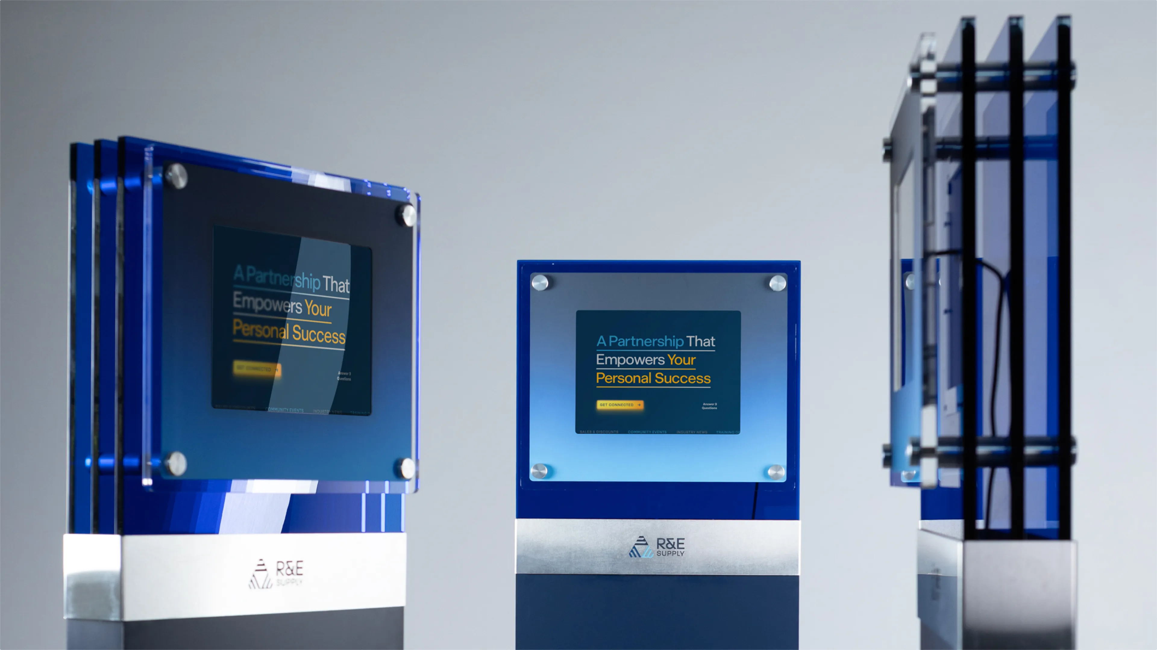 R&E Supply A Partnership That Empowers Your Personal Success dealer program kiosk displays shown in three views including front, angled, and side on grey surface with R&E Supply base plates, web design by Unbound Collective