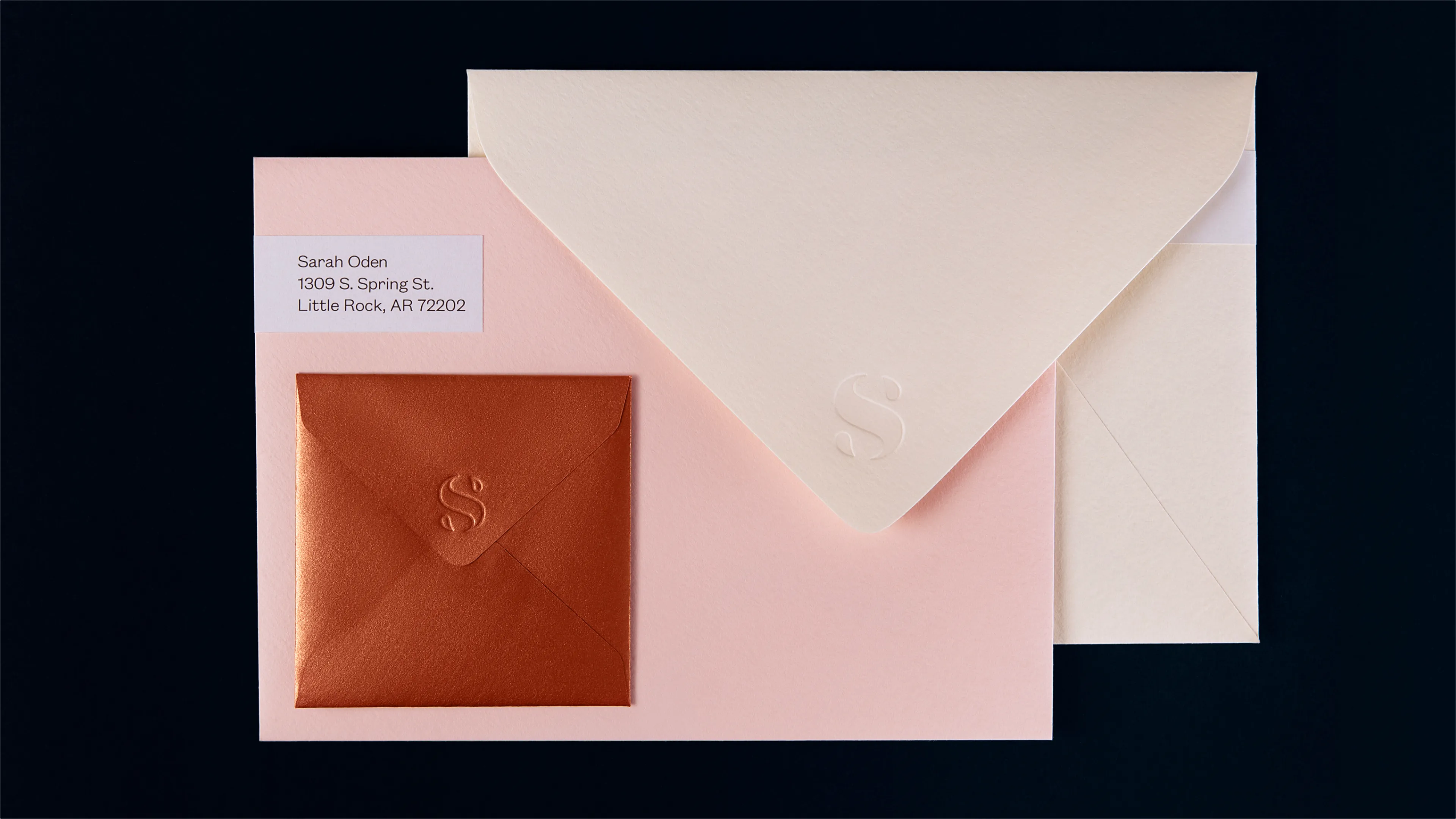 Sarah Oden Photography brand envelope suite showing copper square envelope with embossed S monogram, large cream envelope with blind emboss, and pink envelope with address label on dark background, print design by Unbound Collective