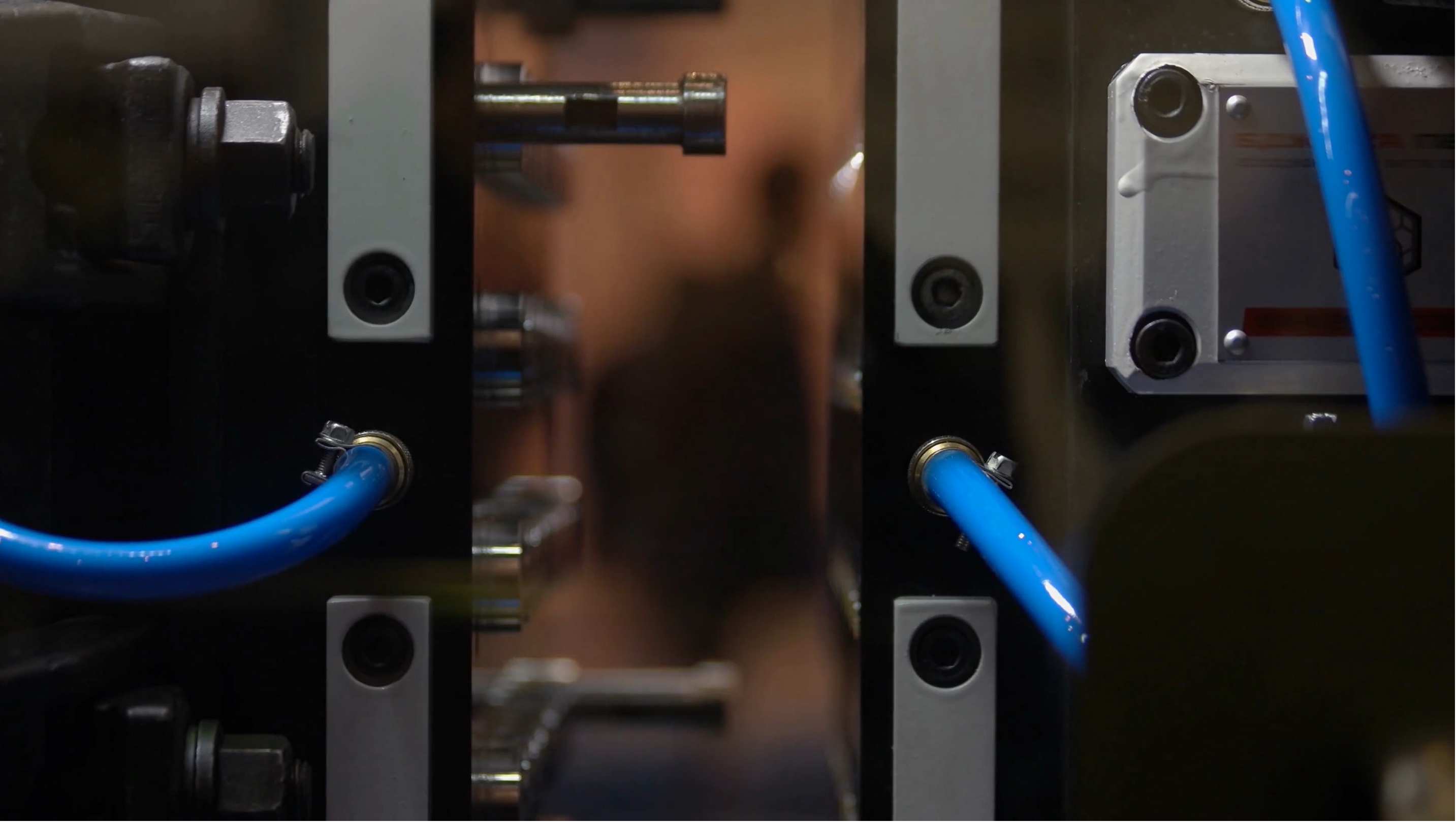 Close-up of industrial injection molding machinery with blue tubes and metal bolts around a central opening.