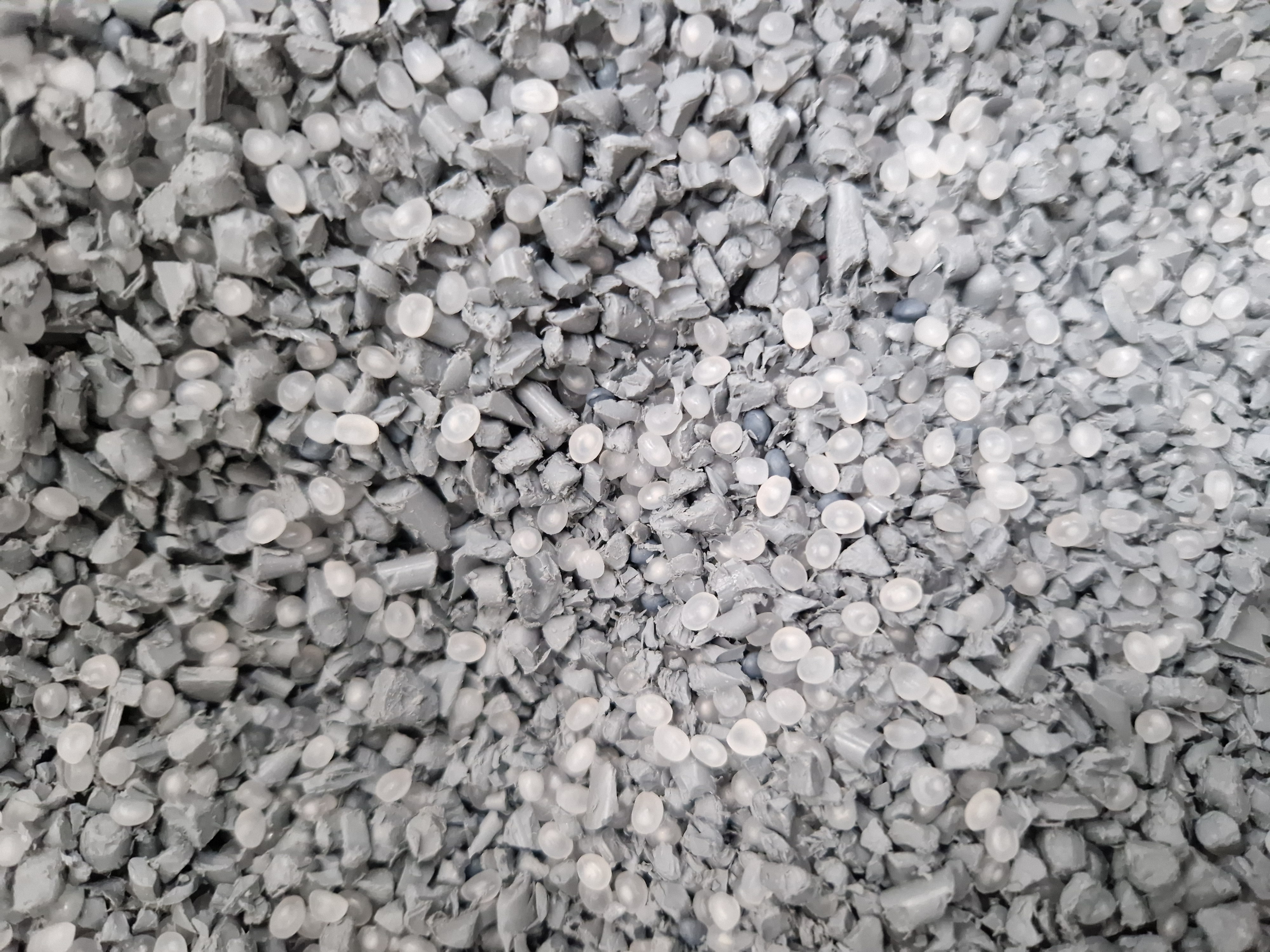 Close-up of small, irregular gray plastic pellets with translucent round beads mixed in.