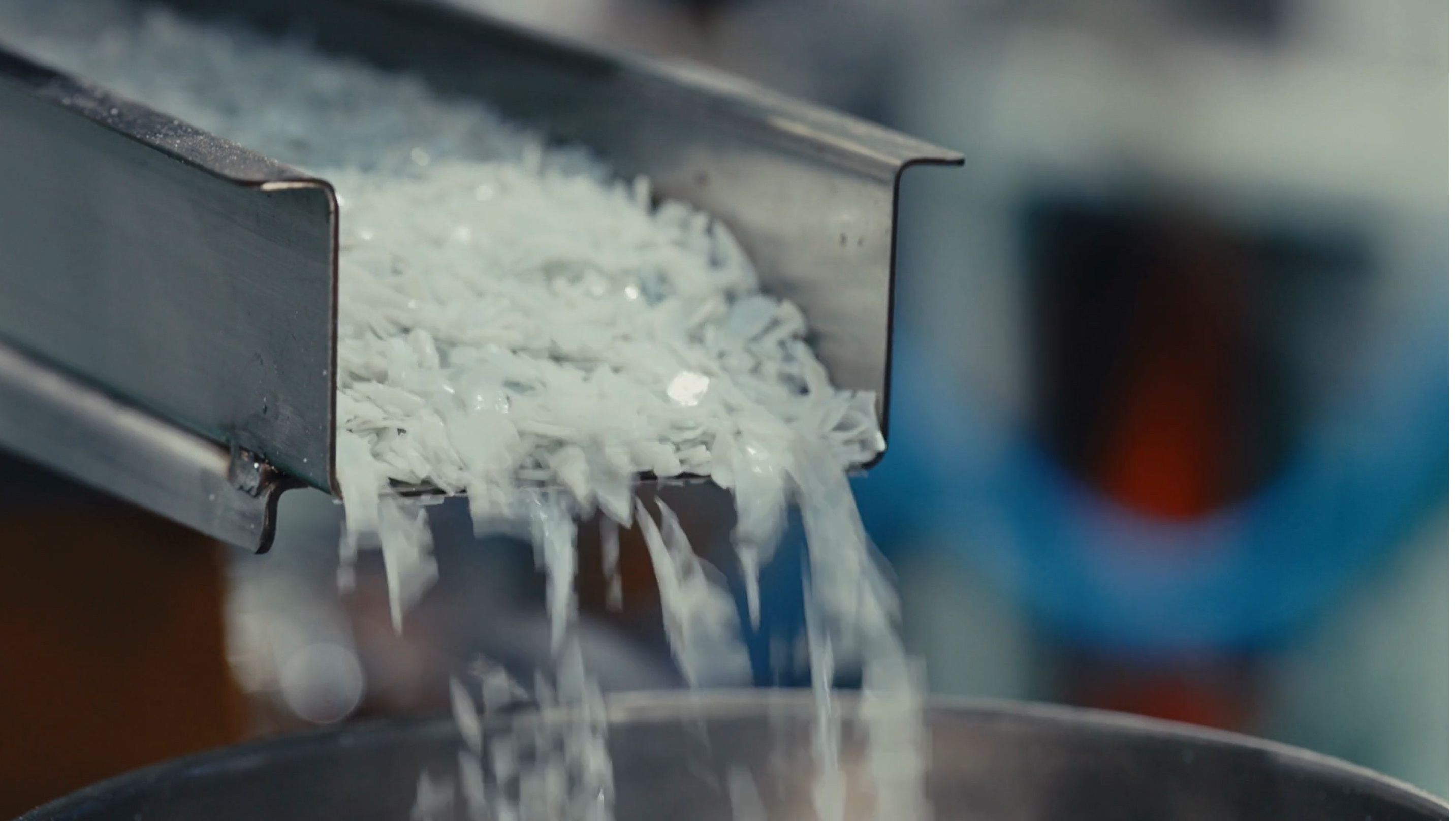 White plastic pellets pouring from a metal chute into a container.