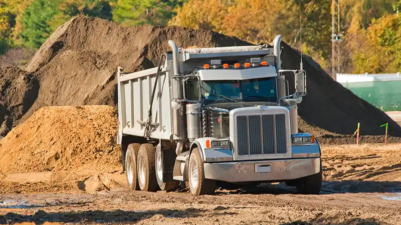 Heavy duty ump truck sitting in a dirt lot picking up a load of dirt.