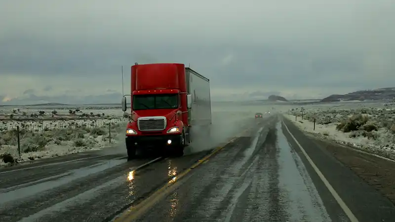 Red semi truck driving down a two lane road in snowy wet conditions