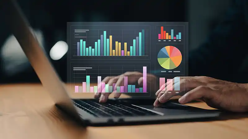 Person sitting at desk working on a computer looking a t charts and graphs