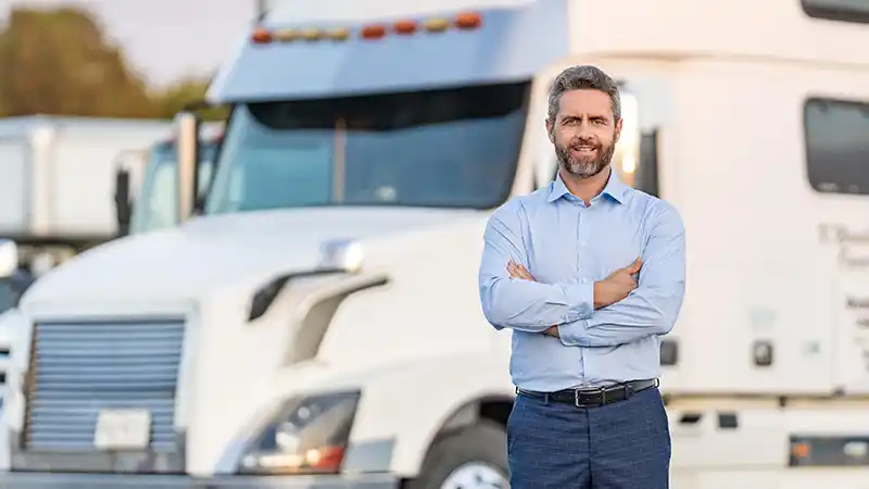 Two semi trucks parked at a growing small fleet yard with an owner nearby.