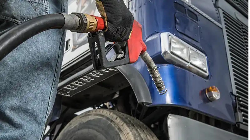 Truck driver fueling a semi at a truck stop while checking fuel prices.