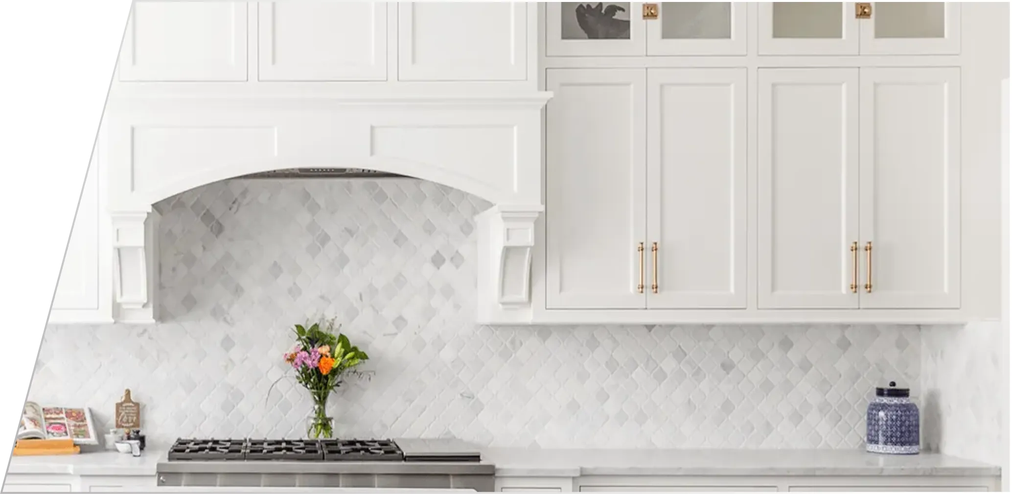 White kitchen with marble backsplash, stainless steel stove, white cabinets, and a vase of colorful flowers on the countertop.