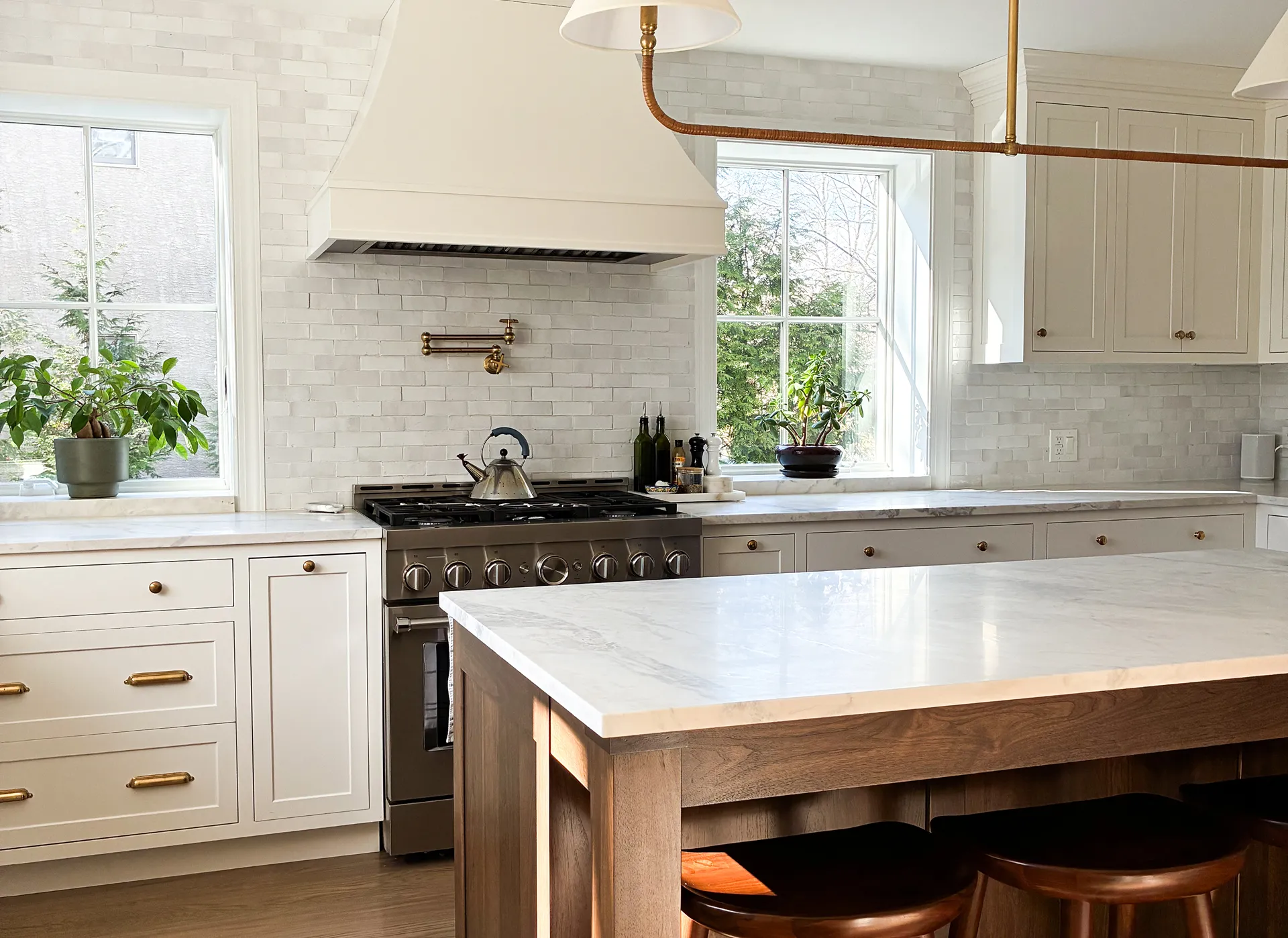 Modern kitchen with white cabinets, a marble-topped island, stainless steel stove, and large windows letting in natural light.