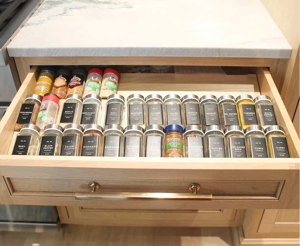 A kitchen drawer neatly organized with labeled spice jars and bottles arranged in rows.