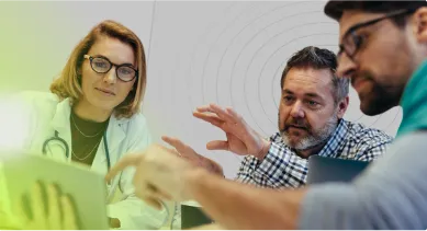 Three diverse medical professionals discussing data around a laptop during a meeting.