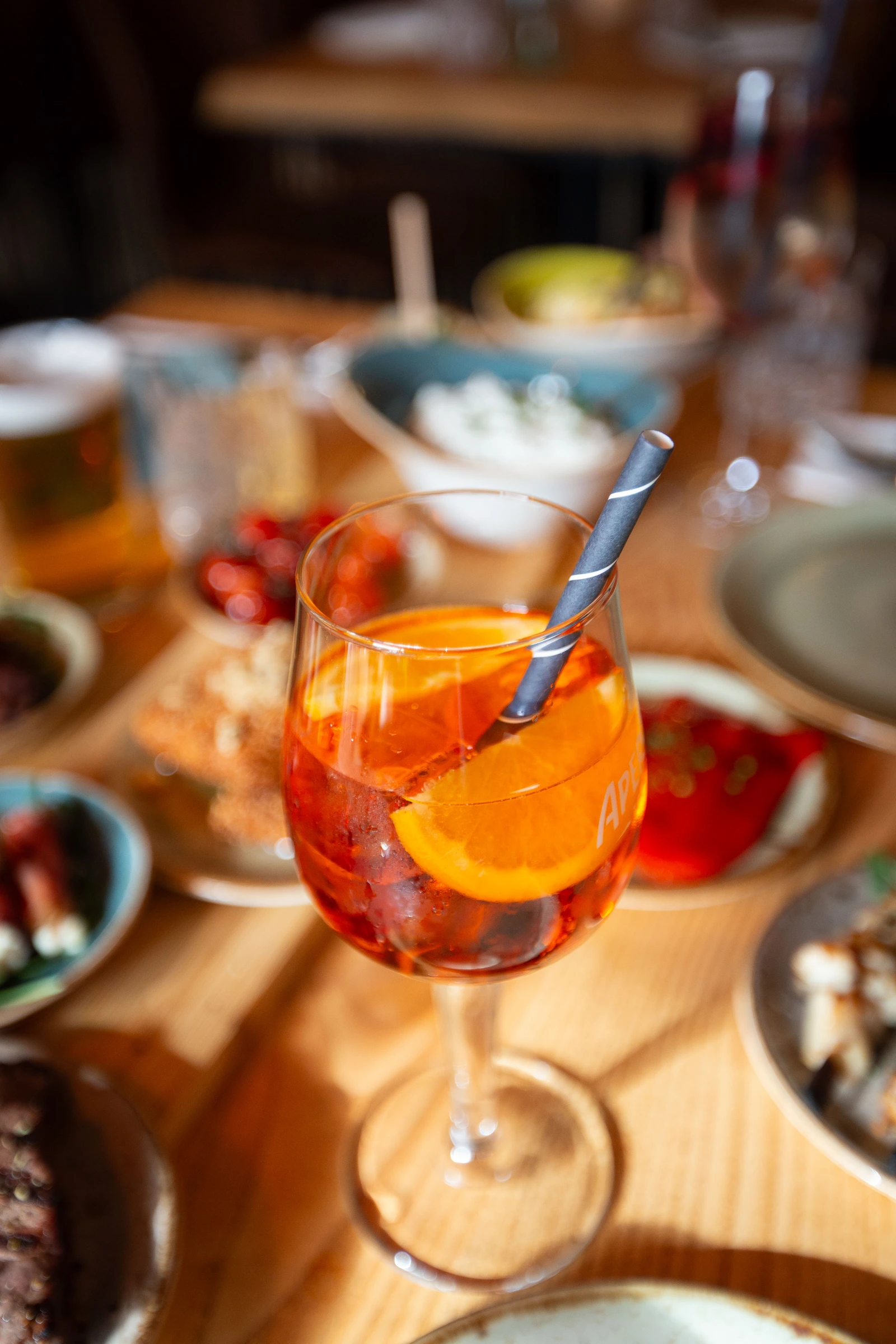 Aperitif mit Orangenscheibe und Strohhalm auf einem gedeckten Tisch mit griechischen Mezedes im Restaurant Mezedes.
