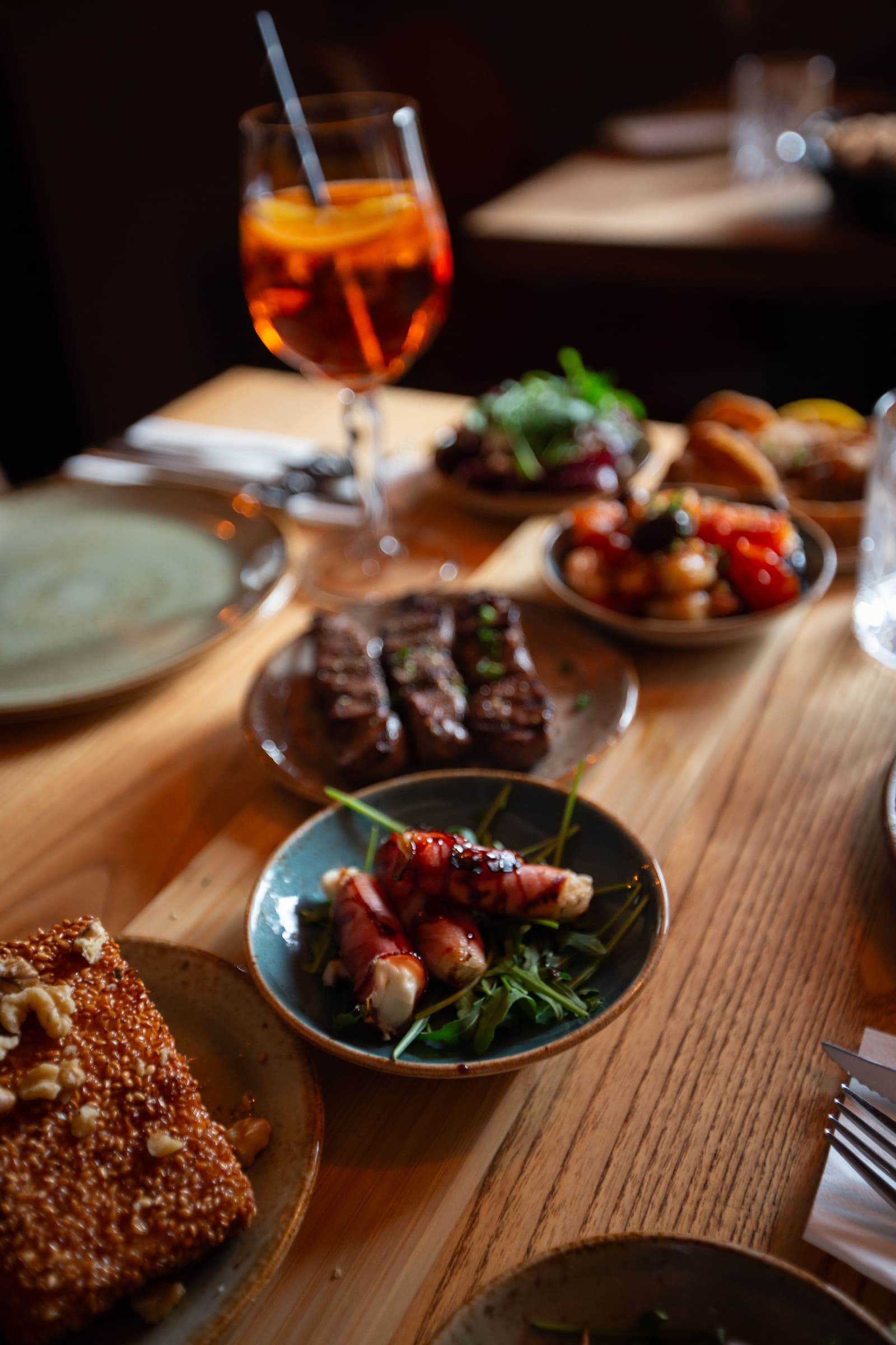 Auswahl griechischer Mezedes mit Speck umwickeltem Käse, gegrilltem Fleisch, Gemüse und Aperitif im Restaurant Mezedes.