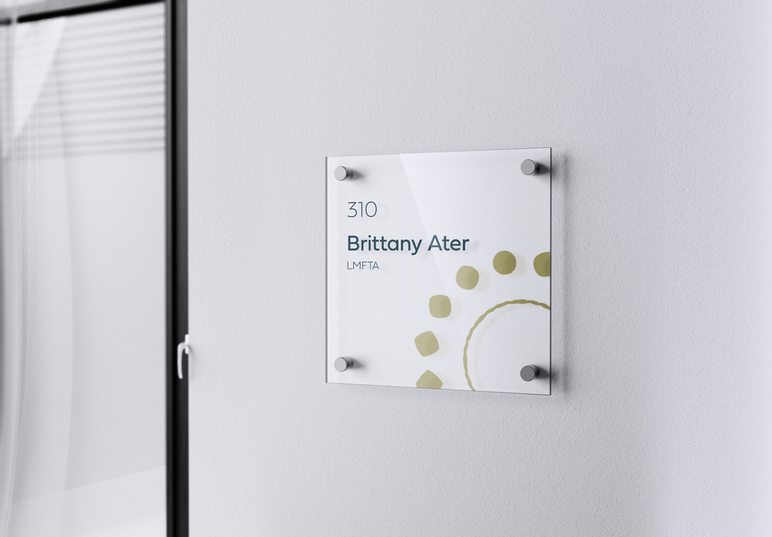 Glass office nameplate on white wall displaying room number 310 and the name Brittany Ater, LMFTA.