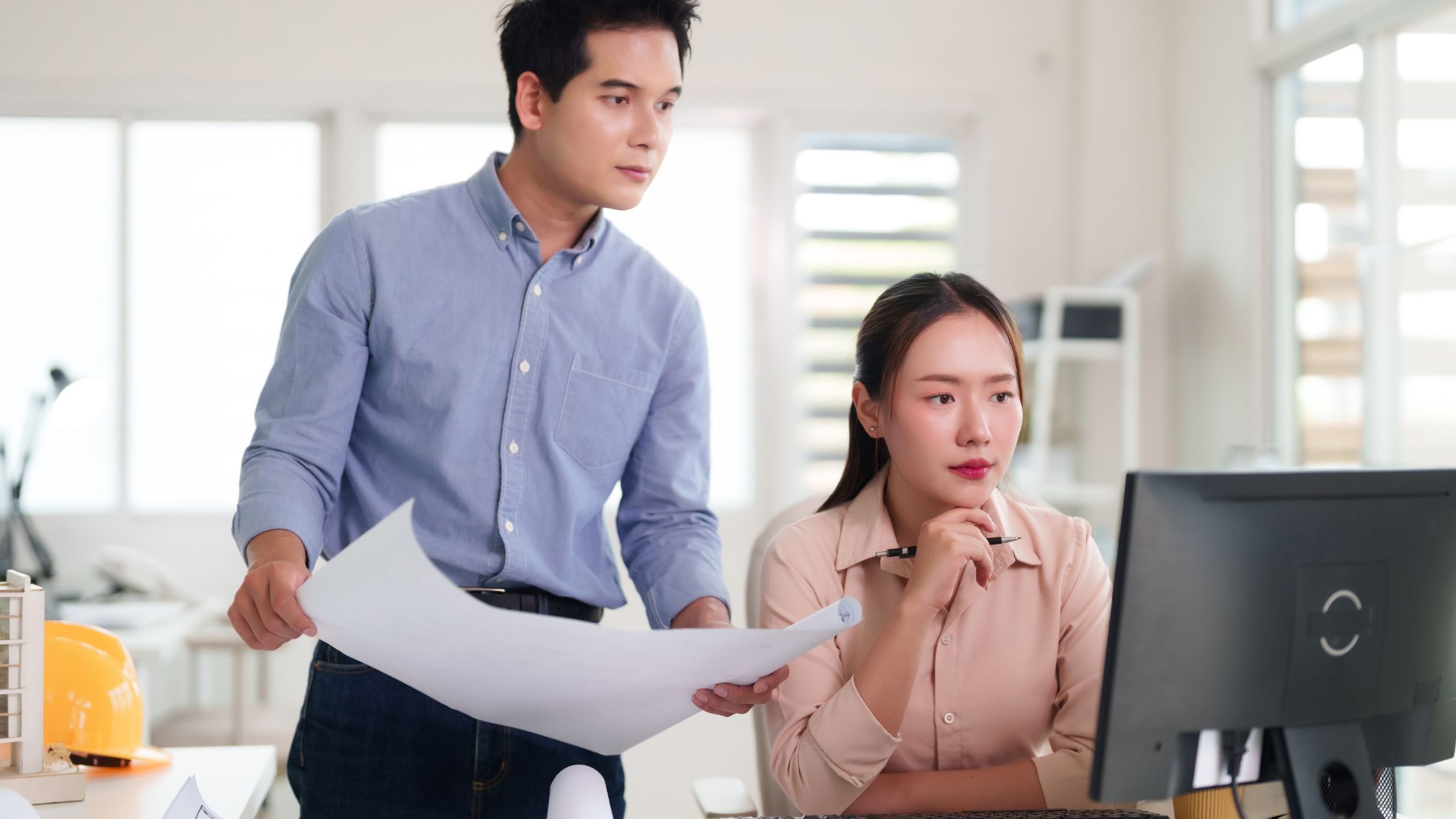Three people work together at a desk, looking at documents and a tablet. 