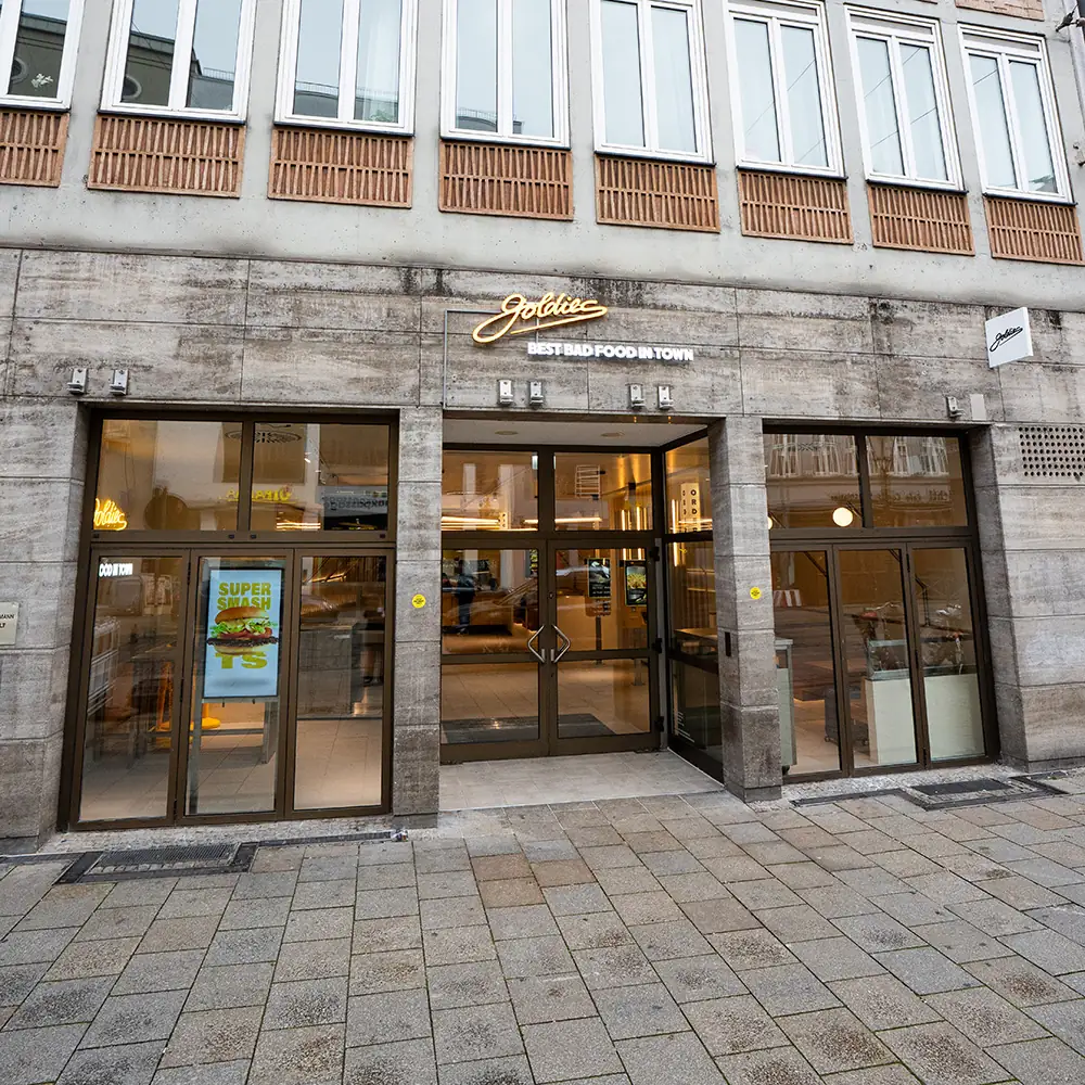 Exterior of Goldies restaurant with large glass windows and a sign stating 'Best Bad Food in Town' above the entrance.