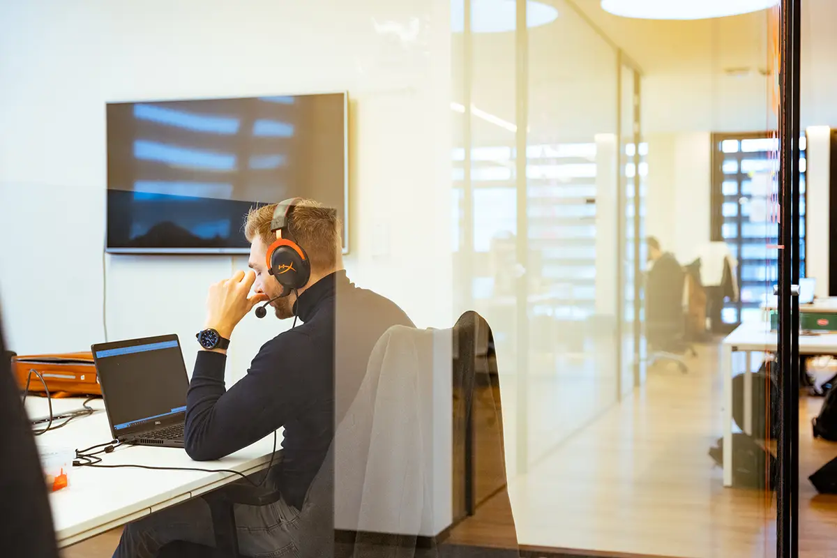 Men behind the desk on a computer wearing headphones