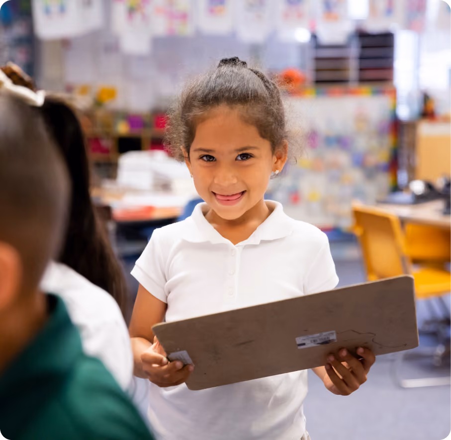 A young girl holding a piece of wood in a classroom.