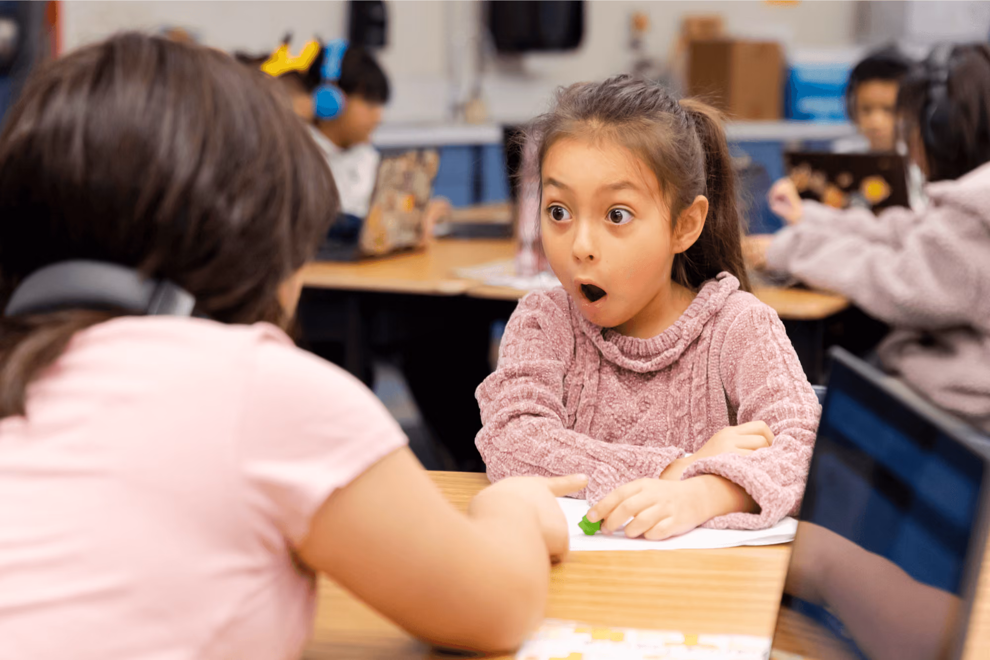 A little girl sitting at a desk with a surprised look on her face.