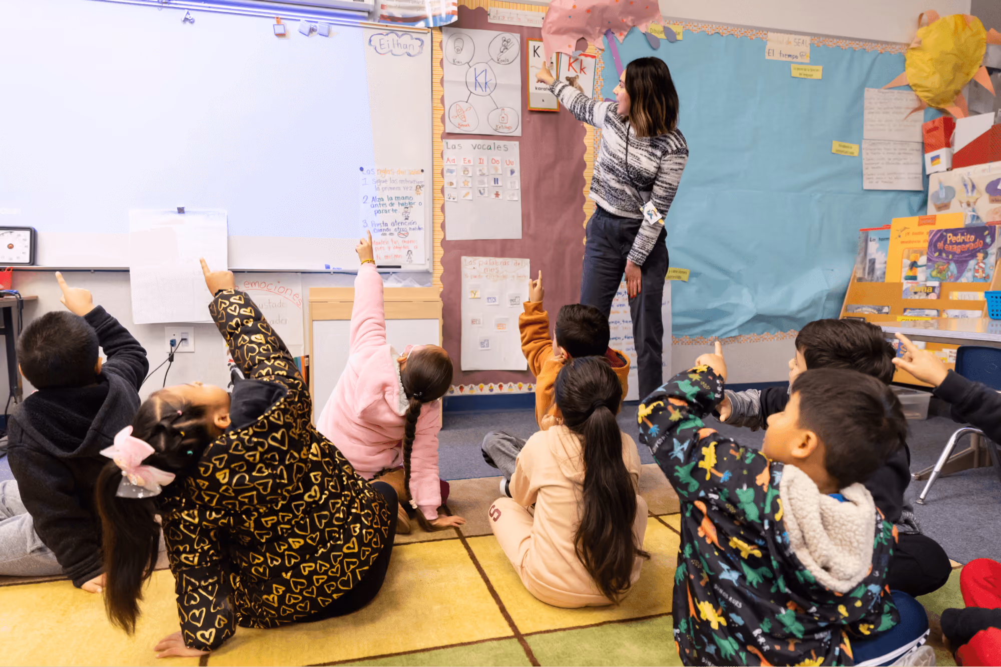 A group of children sitting on the floor in front of a whiteboard.