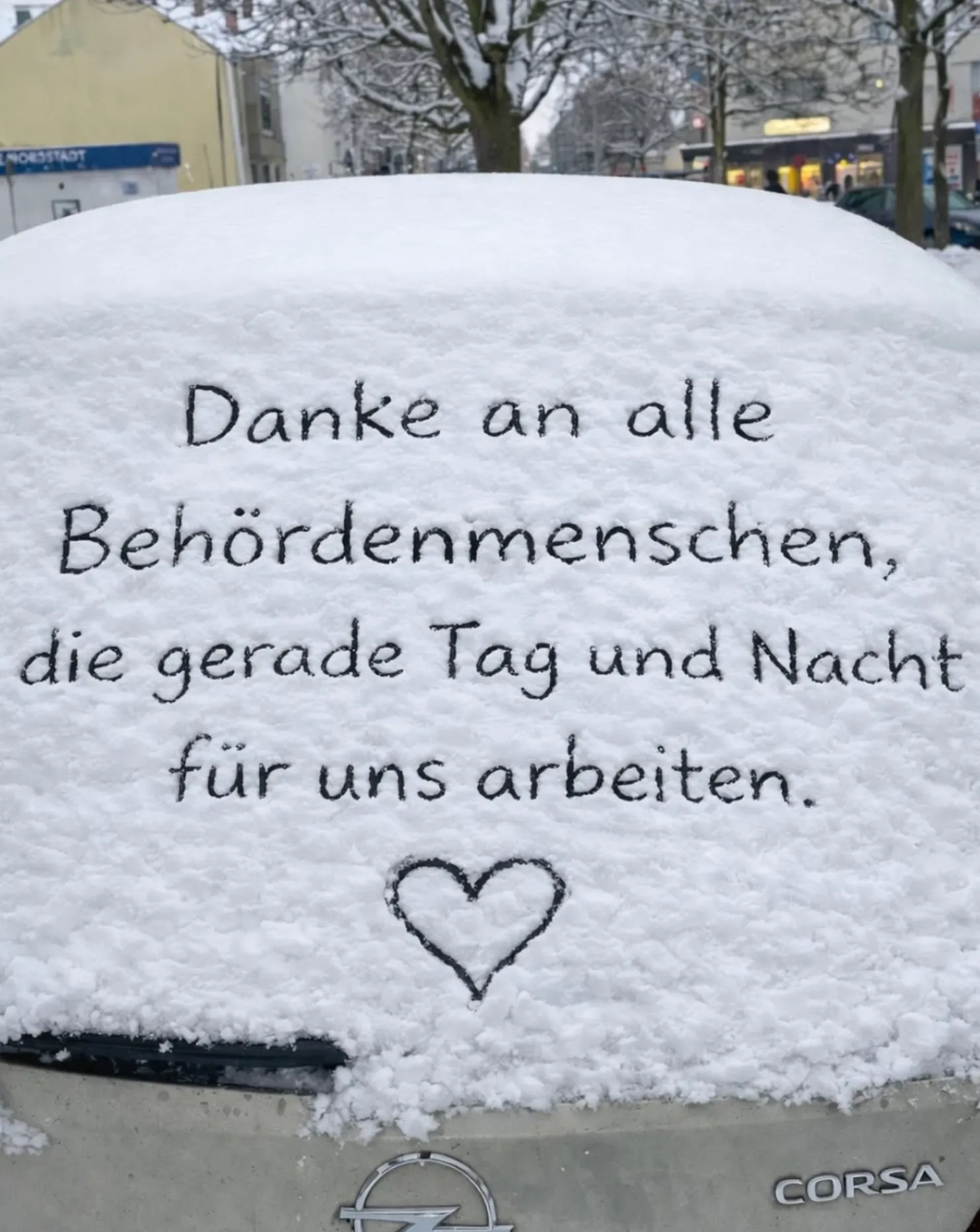 Schneebedeckte Heckscheibe eines Opel Corsa mit der handgeschriebenen Aufschrift: 'Danke an alle Behördenmenschen, die gerade Tag und Nacht für uns arbeiten.' und ein Herz darunter.