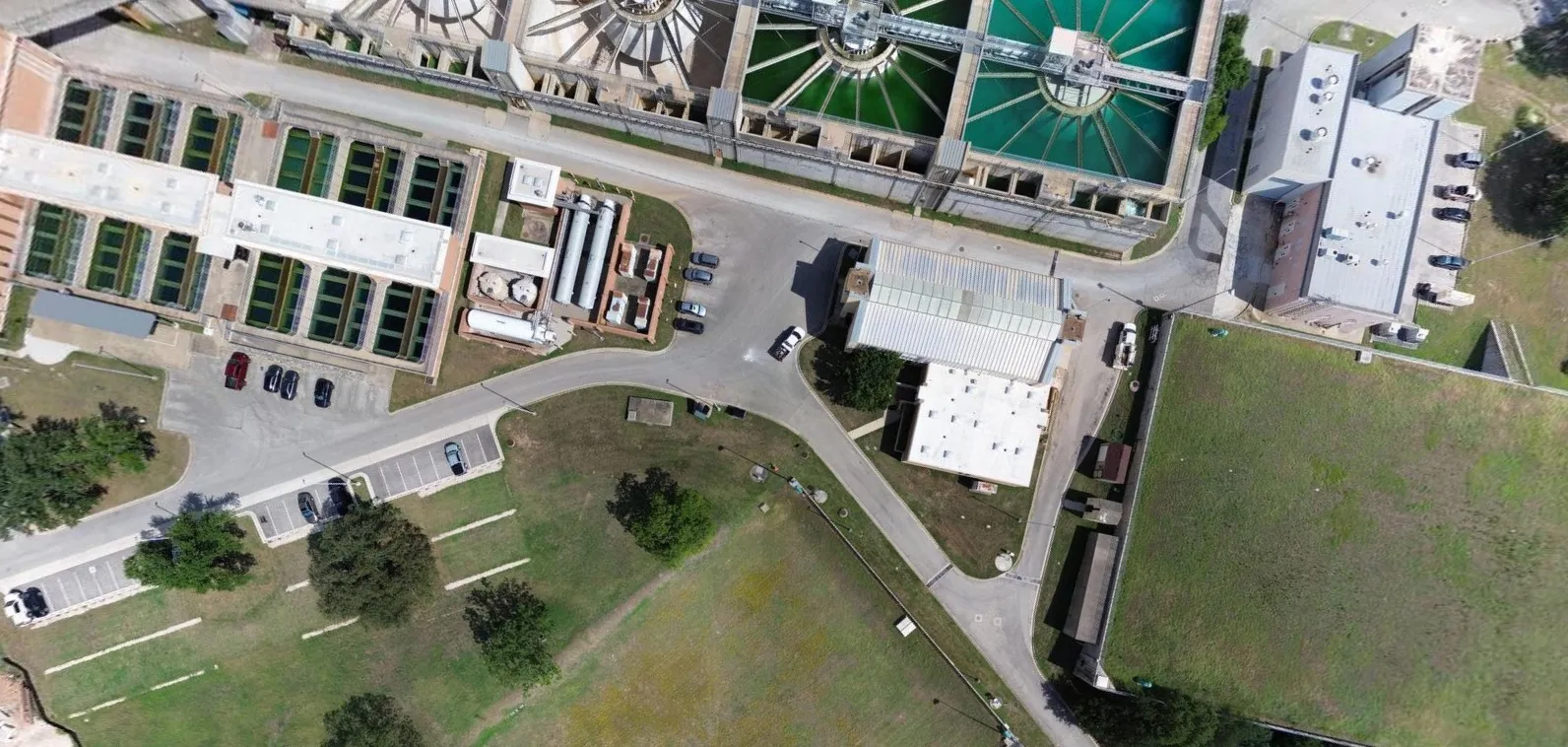 Aerial view of a water treatment plant with circular sedimentation tanks, rectangular filtration basins, several buildings, parking lots, and green lawns.