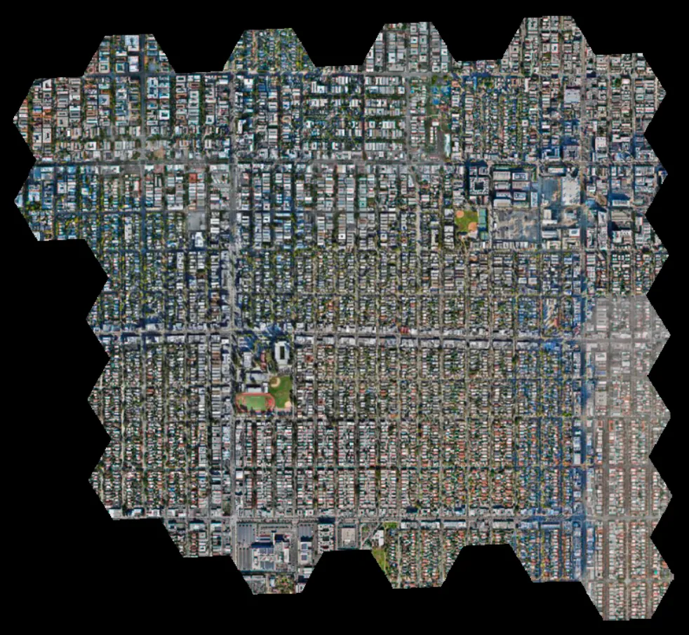 Aerial view of a densely built urban area with a grid-like street pattern, including residential and commercial buildings, and small green spaces with sports fields.