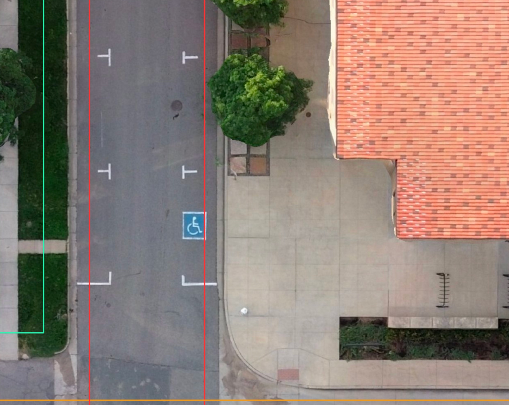 Aerial view of a street with a handicap parking spot next to a building with a red-tiled roof and a tree near the sidewalk.