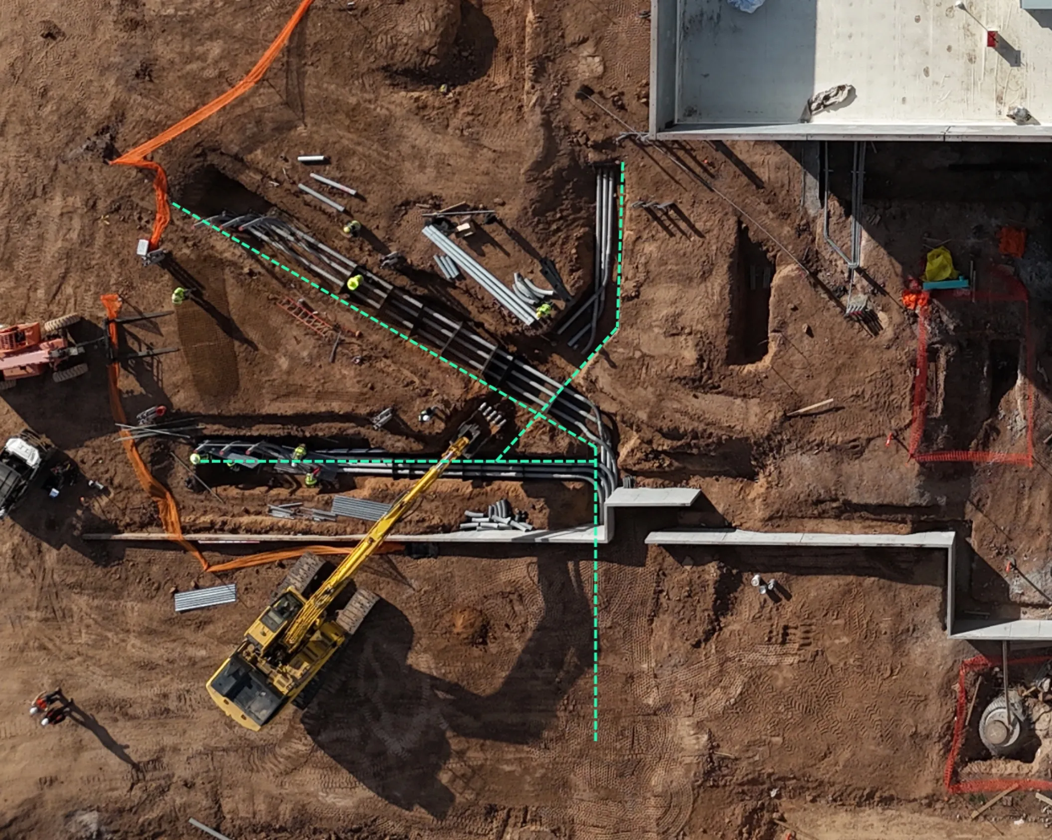 Aerial view of a construction site with a yellow excavator, workers, pipes, and trenches outlined by green dashed lines.