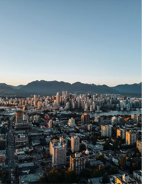 Aerial view of city buildings with mountains in the background under a clear sky at sunset.