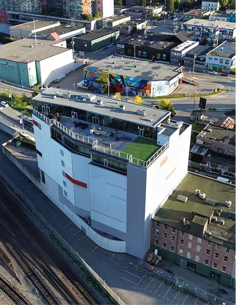 Large white multi-story building with rooftop terrace and urban surroundings including railway tracks and graffiti wall.