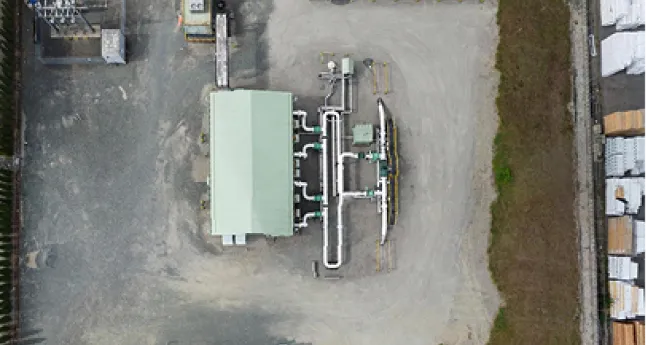 Aerial view of industrial site with a small building and multiple connected pipes on bare ground.