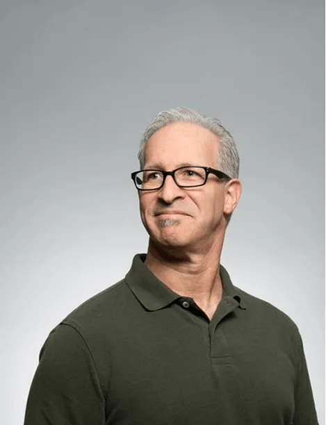 Middle-aged man with gray hair and glasses wearing a dark green polo shirt looking to the side.