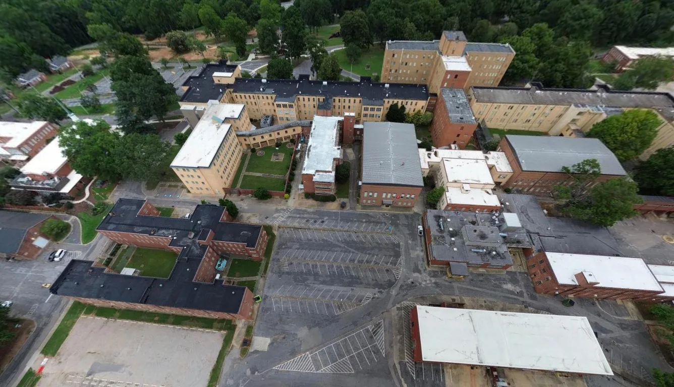Aerial view of multiple connected institutional buildings with parking lots and surrounding greenery.