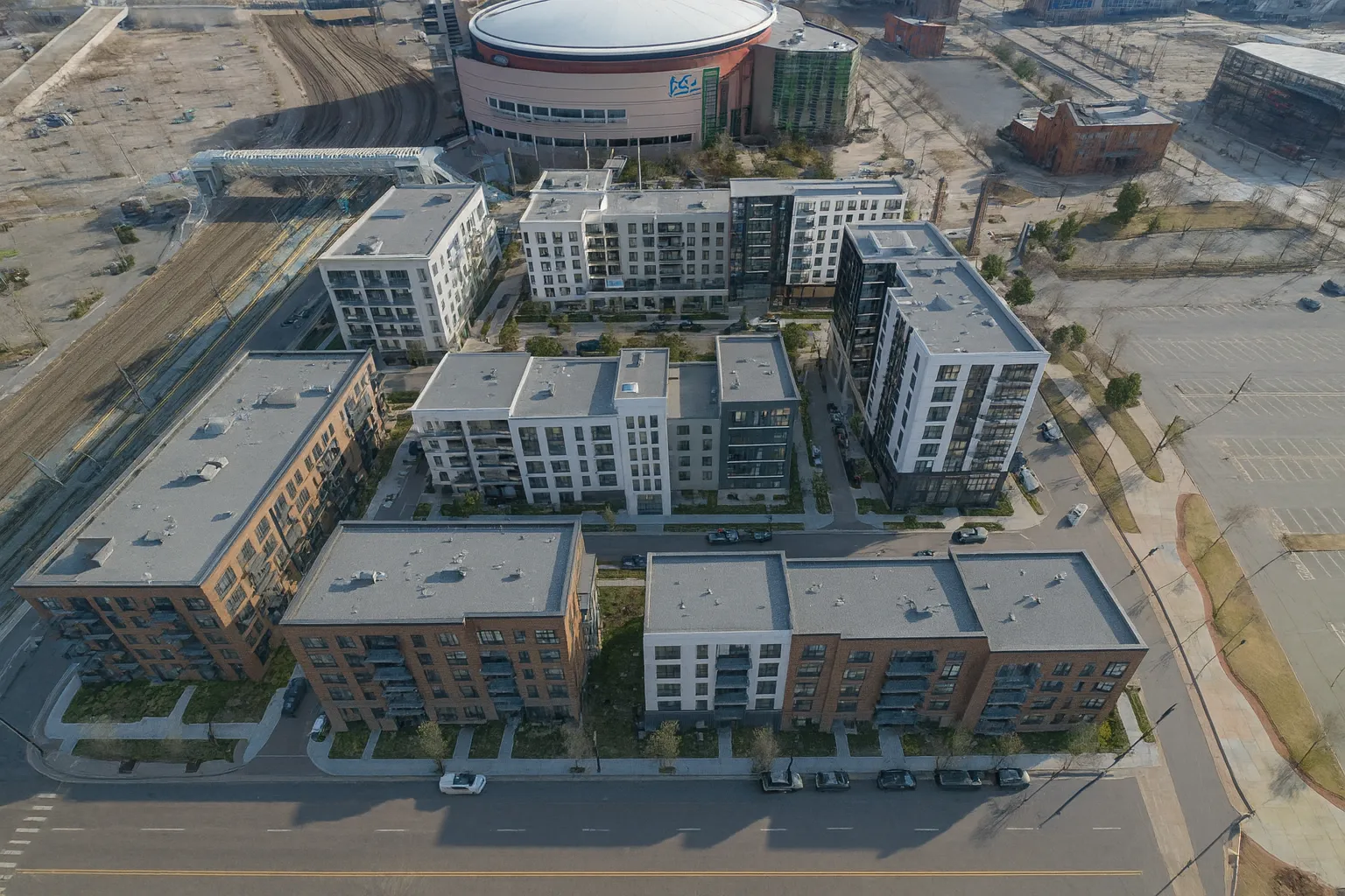 Aerial view of modern apartment complex near empty parking lots and railway tracks.