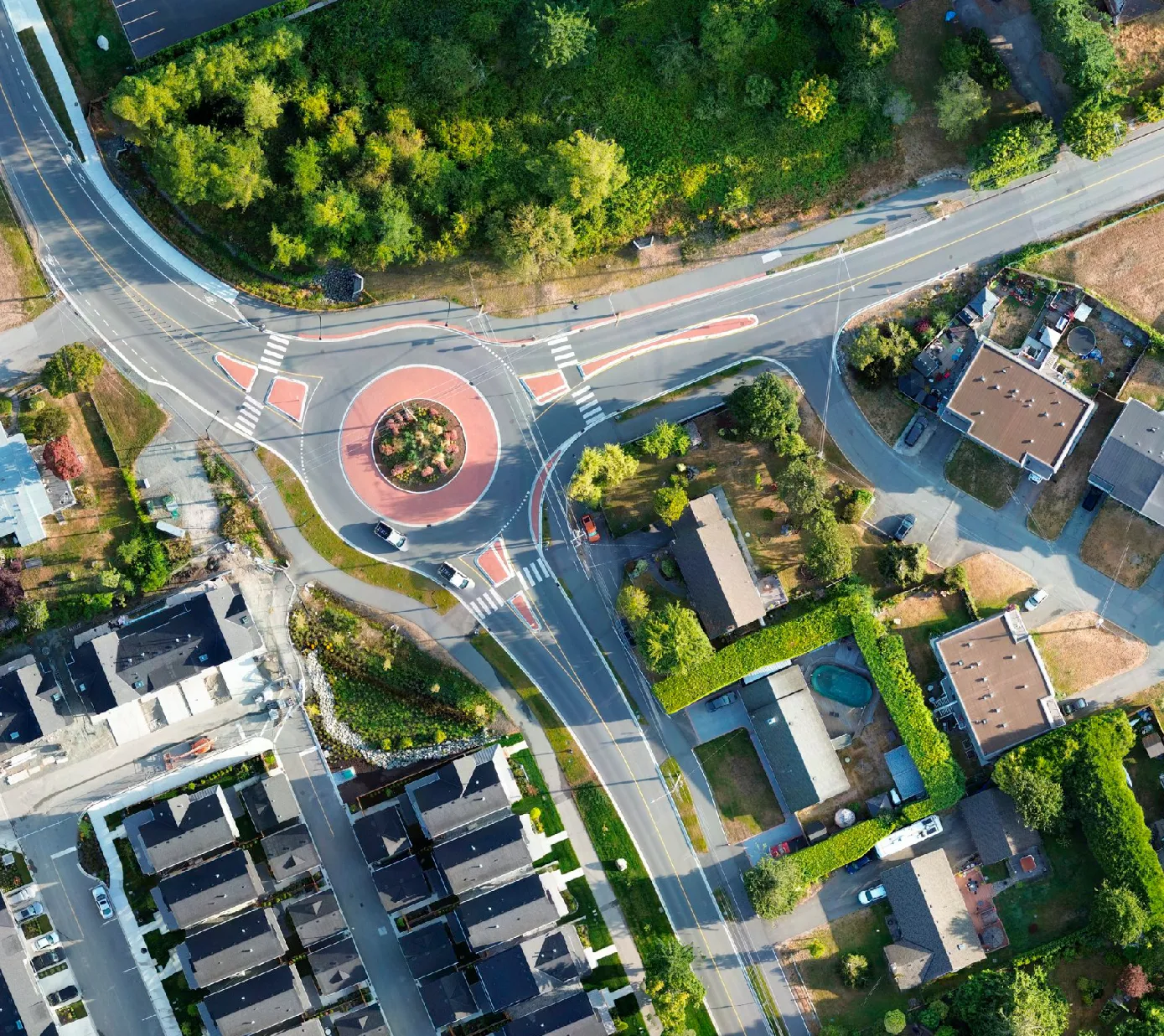 Aerial view of roundabout with landscaped center surrounded by roads, houses, trees, and greenery.
