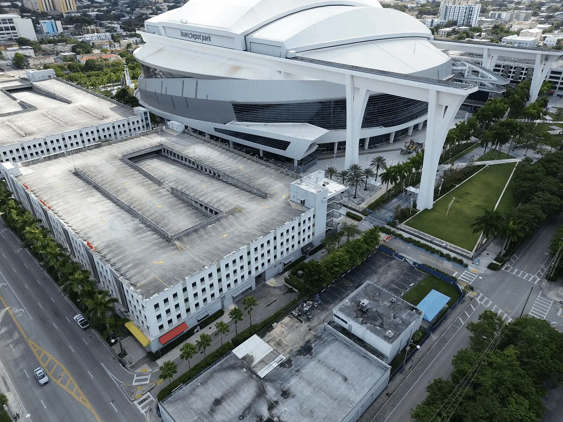 Aerial view of loanDepot Park stadium and adjacent empty multi-level parking garage in an urban area.