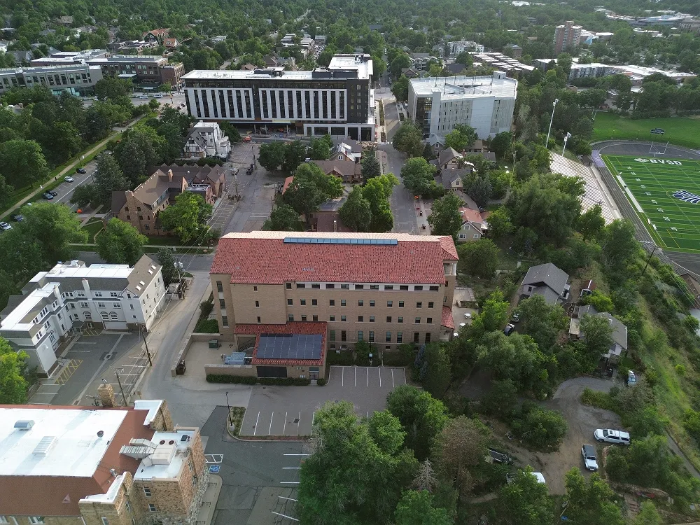 Aerial view of mixed residential and institutional buildings near a sports field surrounded by trees.