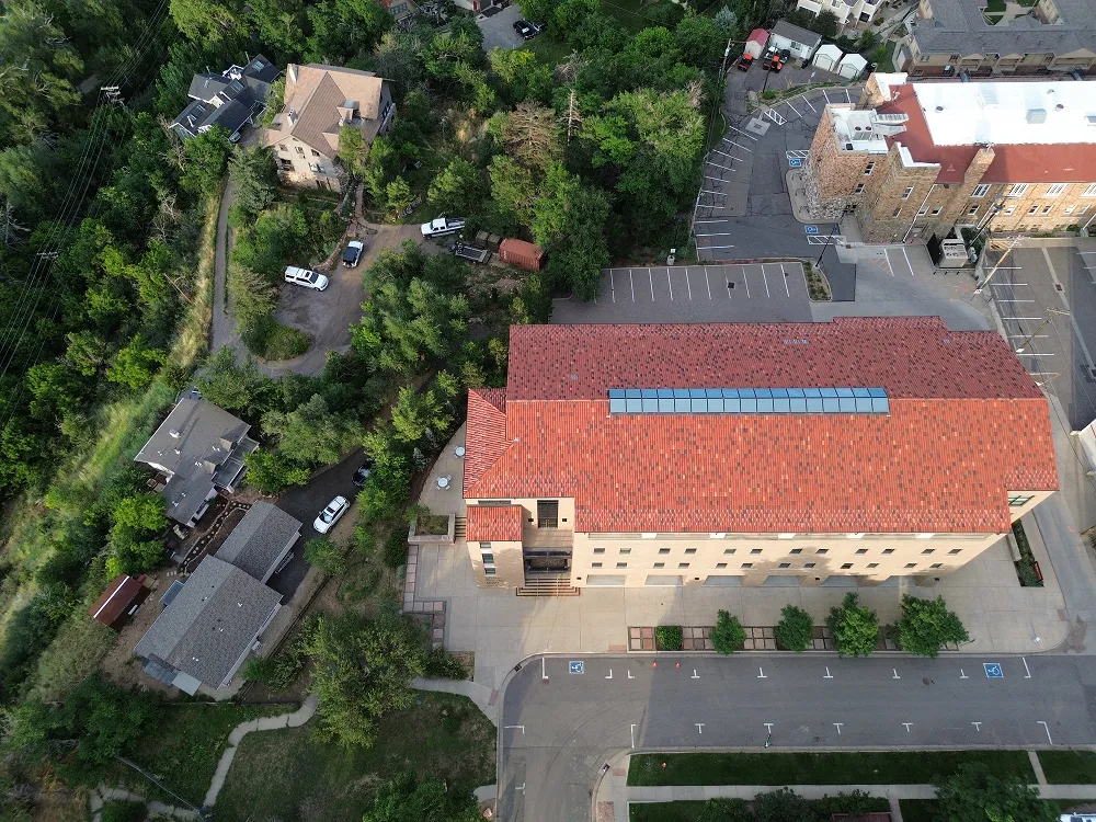 Aerial view of a large building with a red roof surrounded by trees and parking lots.
