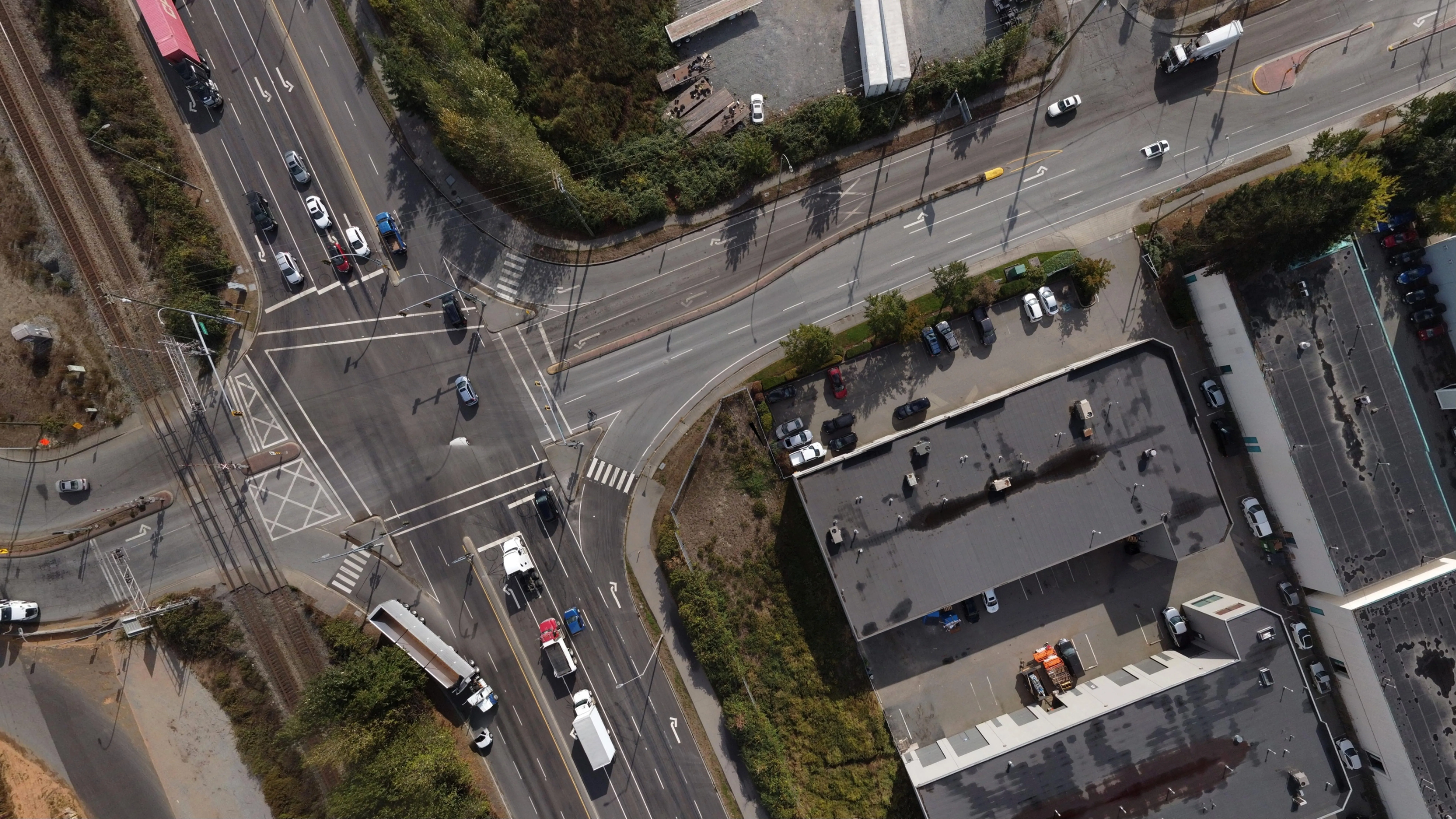 Aerial view of a busy intersection with multiple vehicles, railway tracks, and commercial buildings nearby.