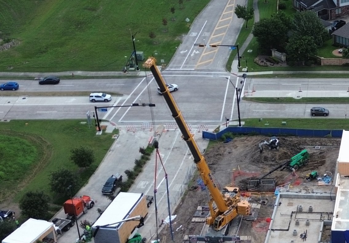 Angled static image of a construction site beside an intersection, with a crane and traffic.