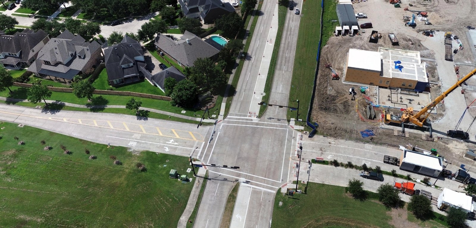 Wide aerial view from above an intersection, looking across homes and a construction site.